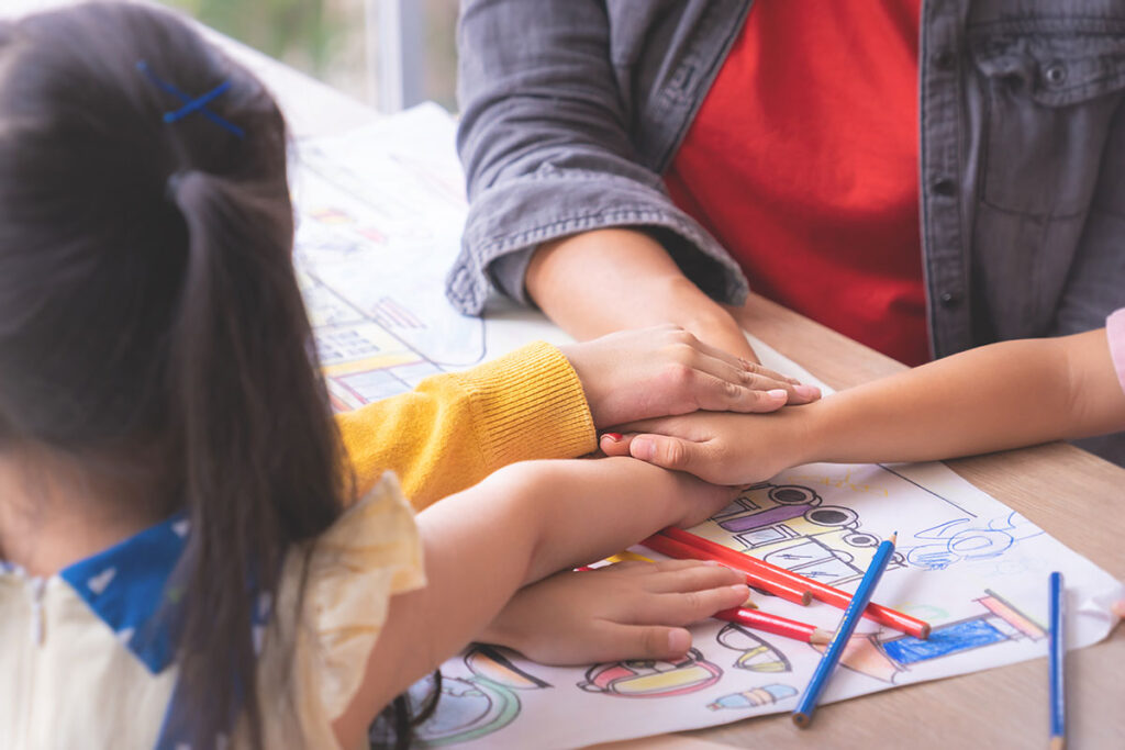 children putting their hands in the center of a desk and an adult is with them