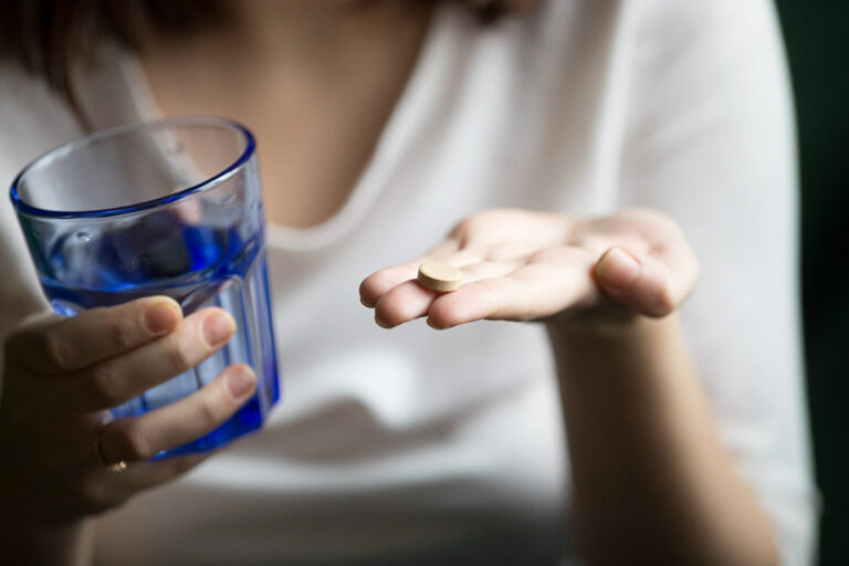 A young woman holding a pill in the palm of her hand and in the other a glass of water